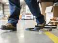 Un trabajador con una puntera composite pisa una cinta de embalaje en un almacén.