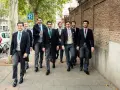 Un grupo de hombres camina por la acera, todos vestidos con trajes elegantes, cumpliendo el **código vestimenta** de un evento formal.