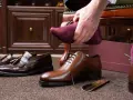 Hombre se pone calcetín morado para ablandar zapatos con crema hidratante. Zapatos de vestir y mocasines en el suelo.