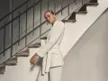 Mujer posando con un elegante outfit blazer blanca, pantalón a juego y cinturón, junto a una escalera antigua.