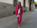 Mujer sonriente luce un espectacular outfit rosa de traje pantalón y blazer, con un cinturón blanco y bolso a juego.