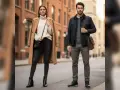 Pareja con estilo urbano. Ella luce un abrigo camel, jersey de cuello alto y pantalones negros con botas. Él, chaqueta azul marino, jersey verde y pantalones grises, con un traje con botas.