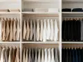 Armario organizado con ropa colgada y doblada en tonos neutros y oscuros. Una clara **estética minimalista** que inspira orden y calma.