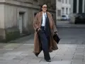 Chica tomboy con abrigo largo marrón, traje de raya diplomática y bolso negro.