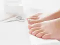 Pies cuidados y herramientas para pedicura sobre toalla blanca.
