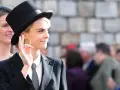 Una mujer tomboy con sombrero de copa y traje negro, con un tatuaje en la mano, saluda a la multitud.