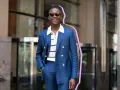 Hombre sonriente con traje azul y camiseta blanca a rayas, gafas de sol, posando con la mano en el bolsillo.