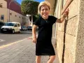 Mujer sonriente con vestido negro, apoyada en pared de piedra. Sus medidas cuerpo mujer son únicas y hermosas.