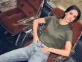 Mujer con vaqueros y polo verde, sentada en una silla de terciopelo, encarnando la moda atemporal.