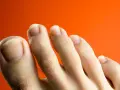 Primer plano de unos pies con uñas amarillas sobre fondo naranja.