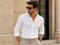 Hombre con gafas de sol y un elegante outfit de camisa blanca y pantalones beige, posando con confianza.