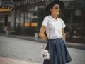Mujer con estilo preppy, luce un polo blanco, falda azul y sombrero negro.