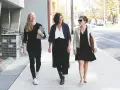 Tres mujeres con atuendo de negocios caminan por la acera, sonriendo y conversando.