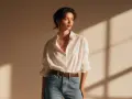 Mujer con camisa blanca arremangada y metida por dentro de sus jeans, cinturón marrón y collar dorado.