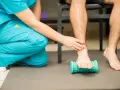 Fisioterapeuta ayuda a un paciente a aliviar el dolor de fascitis plantar con un rodillo de masaje.