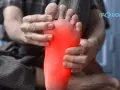 Persona sujetando su pie con dolor, resaltado en rojo.