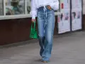 Mujer con camisa blanca y pantalones vaqueros anchos, a la altura de la cintura, con un bolso verde brillante.