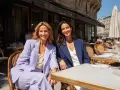 Dos mujeres sonríen sentadas en un café. Una lleva un traje lila, la otra uno azul marino. Ideas para como vestirse para una comunión.