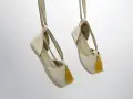 Dos alpargatas de tela beige con pompones amarillos cuelgan de tiras, mostrando su diseño veraniego.