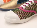 Zapatilla deportiva con malla verde y rosa, puntera blanca y suela vulcanizada. Al fondo, un zapato dorado y otro naranja.