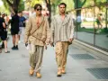 Dos hombres pasean con estilo. Uno lleva un kimono beige y pantalones de lino a rayas. El otro, una camisa a rayas y pantalones beige. Un ejemplo de cómo combinar pantalón lino beige hombre.