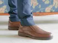 Un hombre viste pantalones azules y unos cómodos mocasines marrones, perfectos para cualquier ocasión.