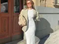 Mujer con blazer y vestido largo blanco, bolso tejido y gafas de sol, posando frente a una puerta de madera.
