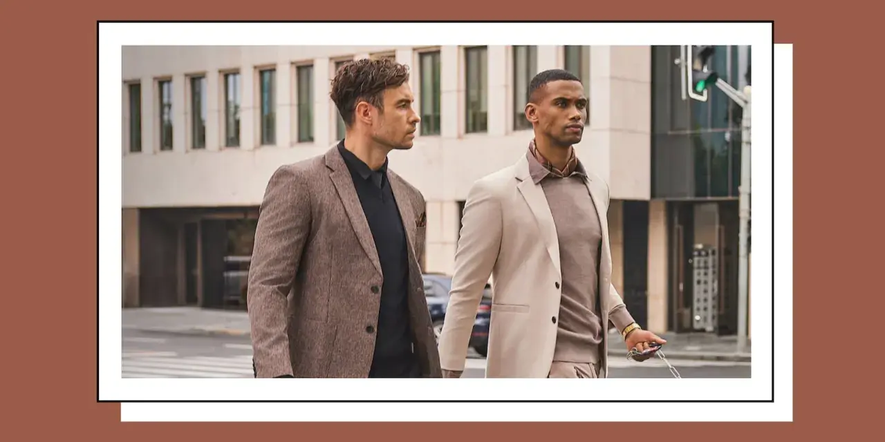 Dos hombres con trajes elegantes caminan por la calle. Uno lleva un traje beige y el otro un traje marrón.