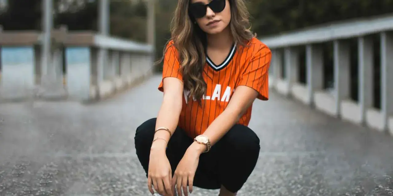 Mujer con estilo smart casual, con camiseta naranja a rayas, pantalones negros y zapatillas deportivas.