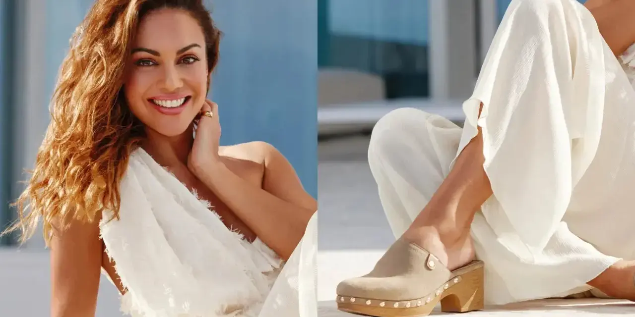 Mujer sonriente con vestido blanco y un pie calzado con zuecos de ante beige, adornados con tachuelas.