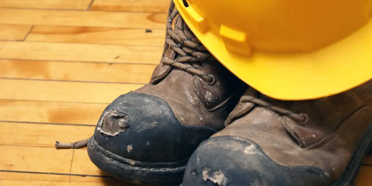 Botas de seguridad desgastadas y un casco amarillo, listos para lavar en lavadora.