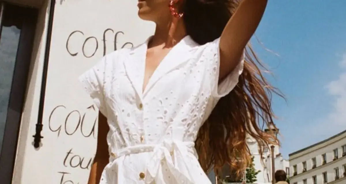 Mujer con un elegante outfit entrevista de trabajo verano, vestido blanco bordado, pendientes rojos, cabello suelto.