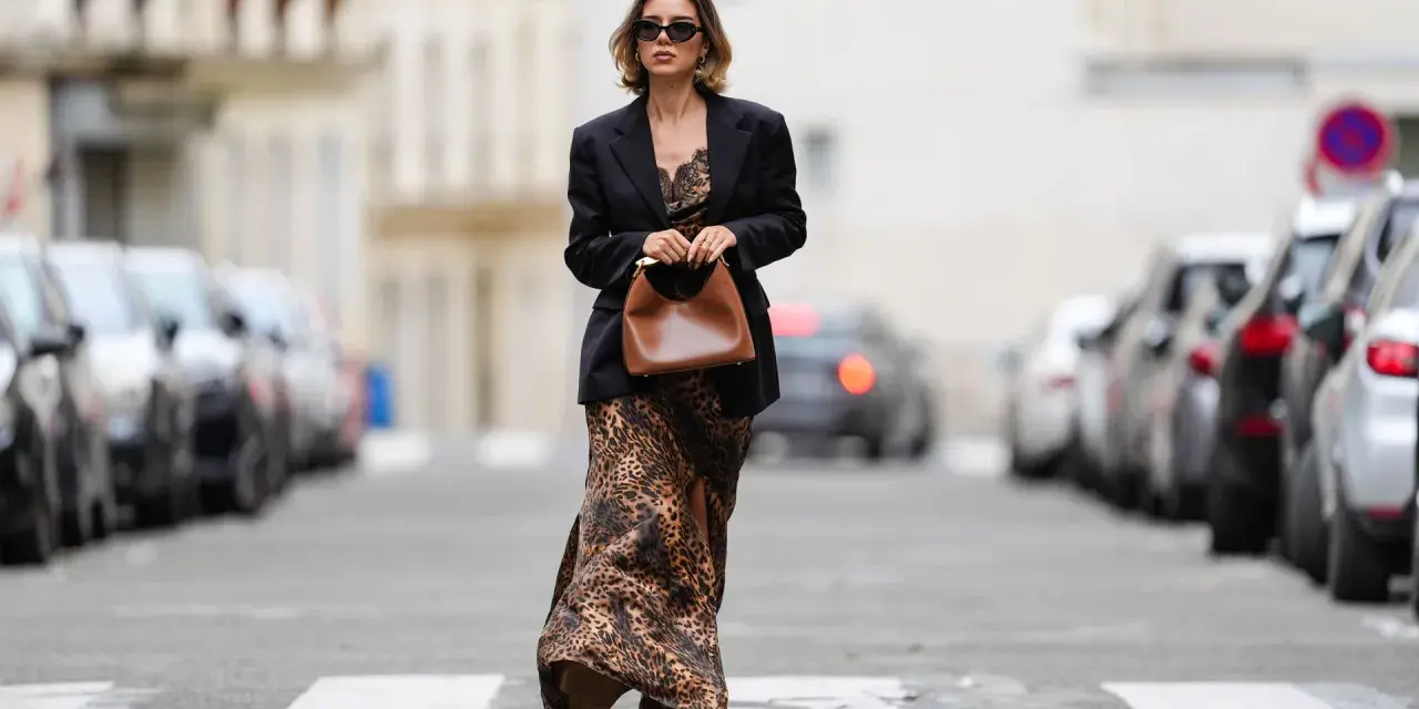 Mujer con un elegante outfit de domingo primavera: vestido largo de leopardo, blazer negro y bolso marrón.