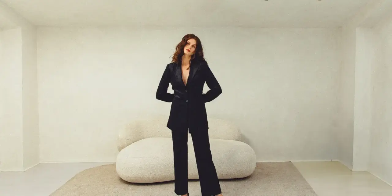 Mujer con elegante traje negro, parte de una colección de **monochrome outfits**. Posando con confianza en un estudio minimalista.