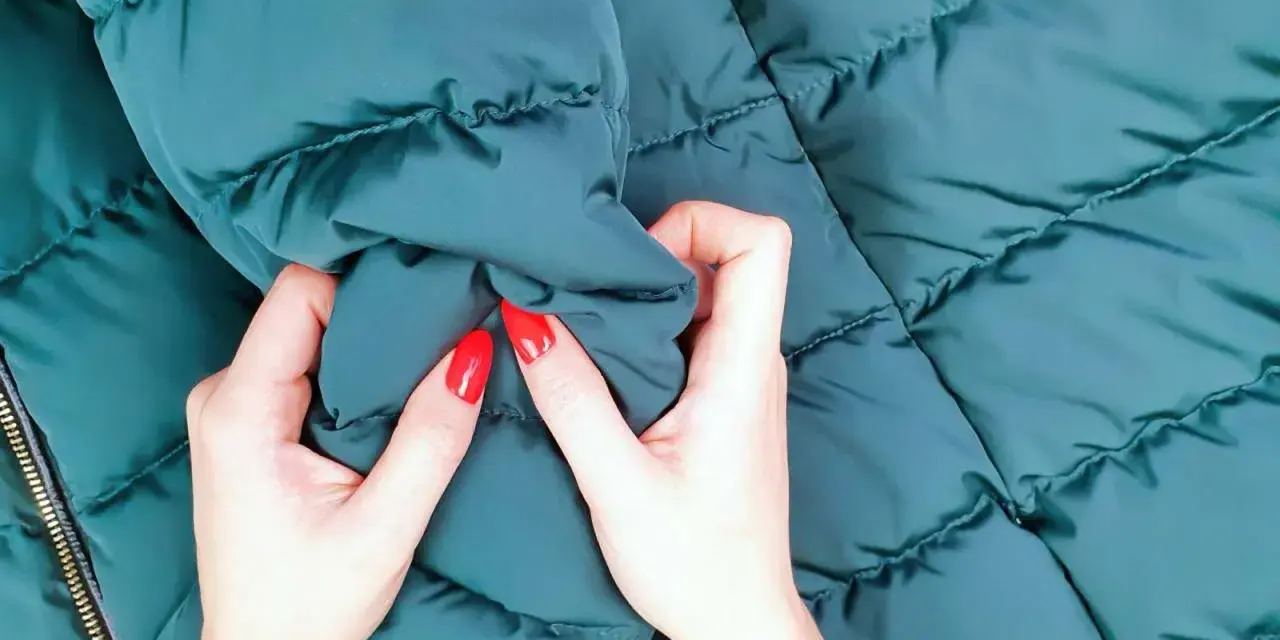 Manos con uñas rojas arrugan una chaqueta verde oscuro. ¡Por fin he lavado un plumas en la lavadora y está como nuevo!