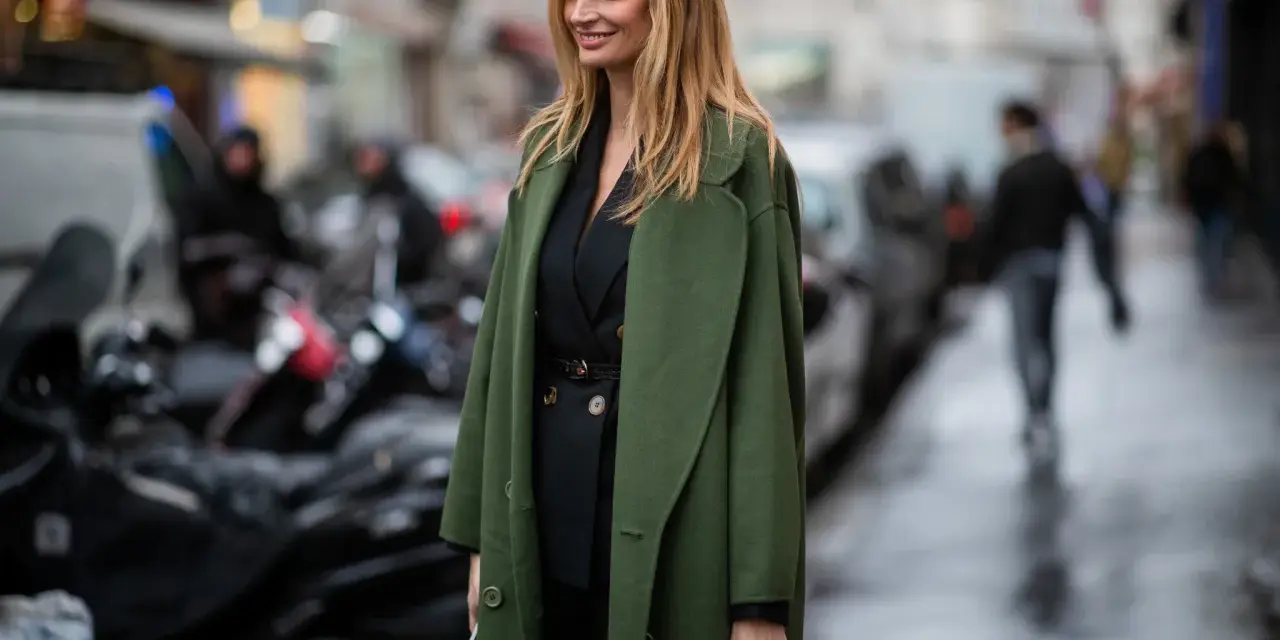 Mujer con traje negro y un abrigo verde olivo, ideal para saber qué abrigo llevar con traje mujer.