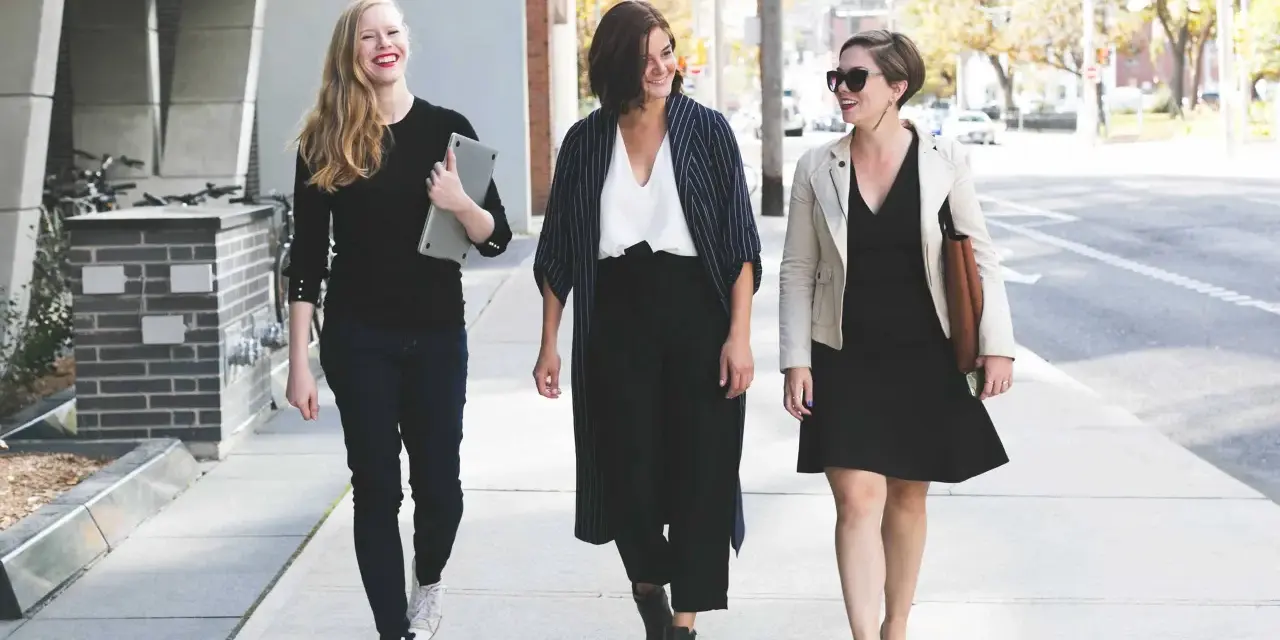 Tres mujeres con atuendo de negocios caminan por la acera, sonriendo y conversando.