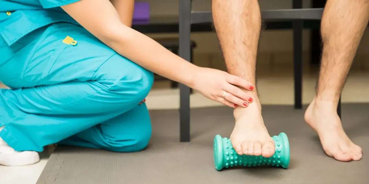 Fisioterapeuta ayuda a un paciente a aliviar el dolor de fascitis plantar con un rodillo de masaje.