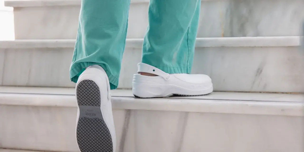 Persona subiendo escaleras con zapatos blancos, mostrando la suela antideslizante. El poliuretano en zapatos ofrece comodidad y durabilidad.