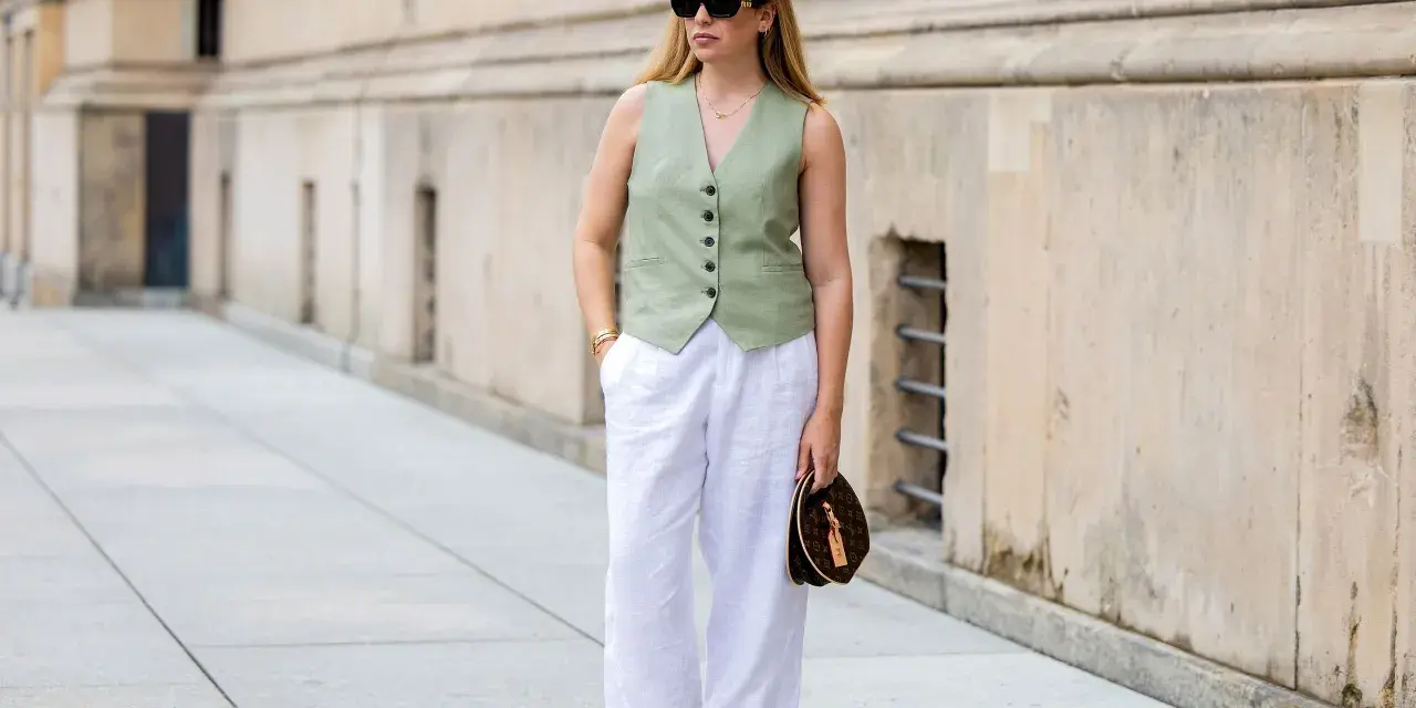 Mujer con un outfit de chaleco verde y outfit pantalon lino blanco, gafas de sol y bolso de mano.