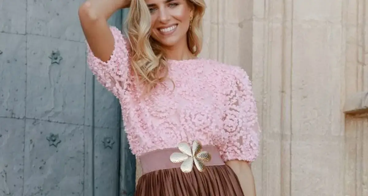 Mujer sonriente con top rosa de encaje y falda marrón, ideal para una boda en octubre, manga corta o larga.