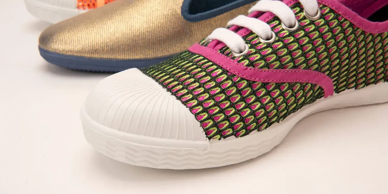Zapatilla deportiva con malla verde y rosa, puntera blanca y suela vulcanizada. Al fondo, un zapato dorado y otro naranja.