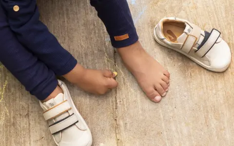 Niño descalzo dibuja con tiza junto a sus zapatos de calzado fisiológico, listos para la aventura.