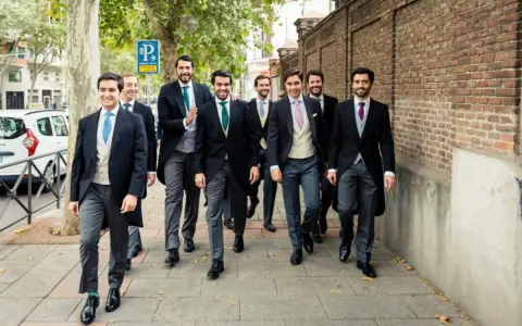 Un grupo de hombres camina por la acera, todos vestidos con trajes elegantes, cumpliendo el **código vestimenta** de un evento formal.