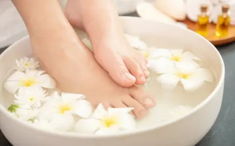 Pies sumergidos en agua con flores blancas, un ritual de spa para probar remedios caseros para quitar el mal olor de los pies.