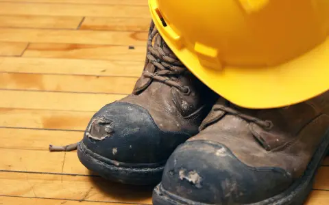 Botas de seguridad desgastadas y un casco amarillo, listos para lavar en lavadora.