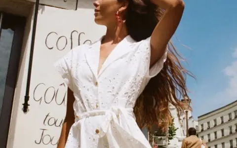 Mujer con un elegante outfit entrevista de trabajo verano, vestido blanco bordado, pendientes rojos, cabello suelto.