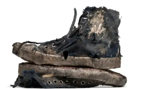 Un par de zapatillas gastadas, rotas y sucias, apiladas una sobre otra. Parecen haber vivido muchas aventuras.