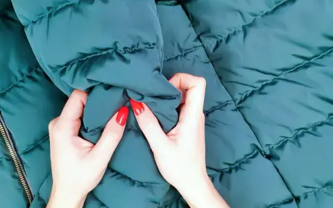 Manos con uñas rojas arrugan una chaqueta verde oscuro. ¡Por fin he lavado un plumas en la lavadora y está como nuevo!