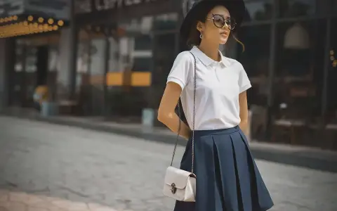 Mujer con estilo preppy, luce un polo blanco, falda azul y sombrero negro.